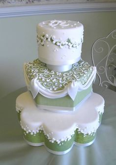 three tiered wedding cake with green and white decorations on top, sitting on a table