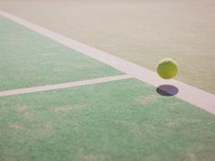 a tennis ball sitting on top of a green court with white lines in the background