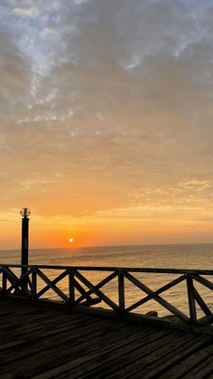 the sun is setting over the ocean with a pier and lighthouse in the foreground