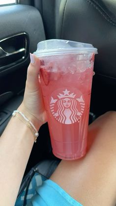 a woman holding up a pink drink in her car