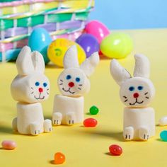 three small plastic rabbits standing next to each other in front of colorful eggs and candies