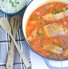 fish stew in a pot with two wooden spoons next to it and rice on the side