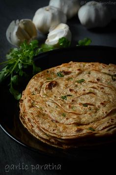 garlic paratha on a black plate next to garlic and parsley sprigs