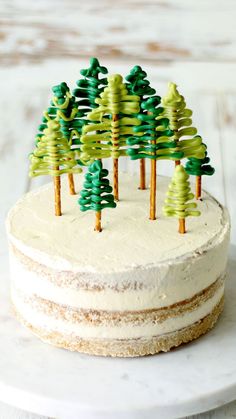 a white cake topped with green trees on top of a marble counter next to a wooden table