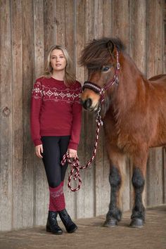 a woman standing next to a brown horse in front of a wooden fence with a red sweater on