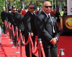 several men in suits and ties standing on a red carpet at an event with barriers around them