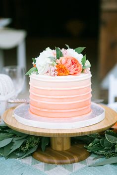 a pink and white cake sitting on top of a wooden table next to greenery