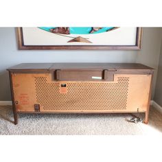 an old radio sitting on the floor in front of a wall with a painting above it