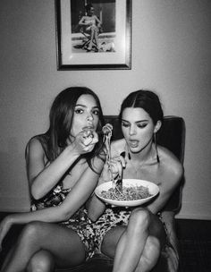 two young women sitting on a couch eating spaghetti and drinking from wine glasses in black and white