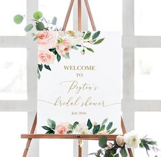 a welcome sign with flowers and greenery is displayed on an easel in front of a window