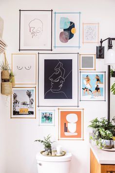 a white toilet sitting in a bathroom next to a wall covered with pictures and plants