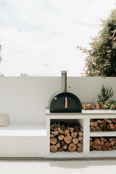 a pizza oven sitting on top of a white table next to a pile of wood