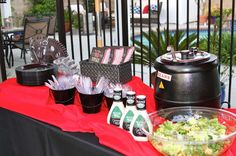 a table topped with salad and drinks on top of a red cloth next to a fence