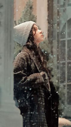 a woman standing outside in the snow with her head turned to look up at something