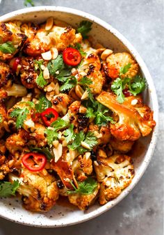 a white bowl filled with cauliflower and red peppers on top of a table