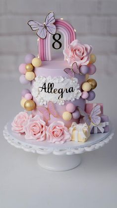 a three tiered cake with pink flowers and butterflies on the top is decorated with an age 8