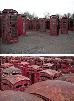 an old red phone booth sitting in the middle of a field full of rusted out cars