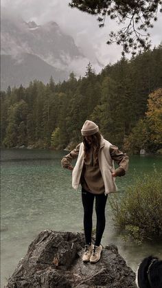 a woman standing on top of a rock next to a lake