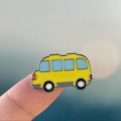 a small yellow bus sitting on top of a persons finger in front of a blurry background