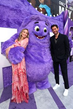 a man and woman standing next to a giant purple monster on the carpet at an event