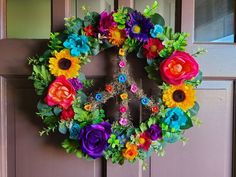 a colorful wreath is hanging on the front door with flowers around it and an iron cross in the center