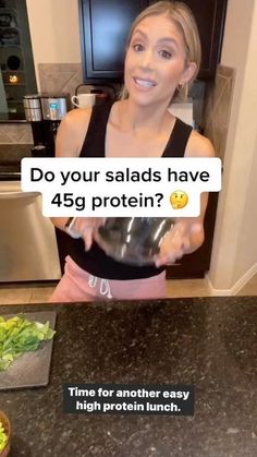 a woman standing in front of a kitchen counter holding a glass bowl filled with lettuce