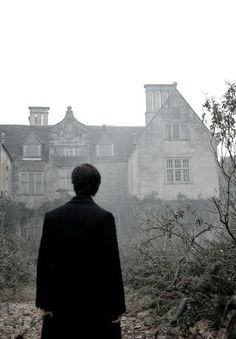 a man standing in front of an old building on a foggy day with trees and bushes