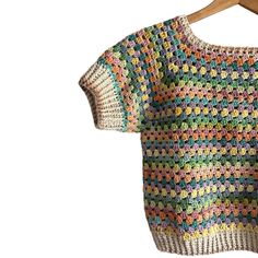 a colorful crocheted sweater hanging on a wooden hanger with clothes pins attached to it