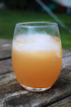 a glass filled with liquid sitting on top of a wooden table next to a grass covered field