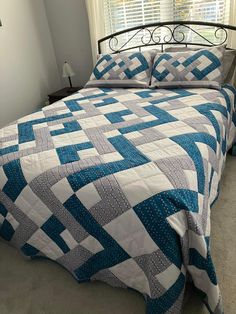 a bed with a blue and white quilt on it's headboard next to a window