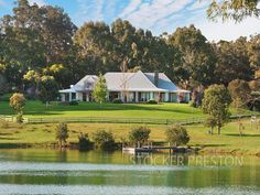 a large house sitting on top of a lush green field next to a lake in front of a forest