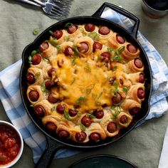 a skillet filled with hot dogs and cheese on top of a blue checkered table cloth