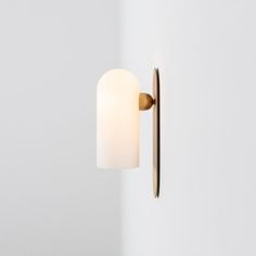 a wall mounted light with a white glass shade on it's side and a gold metal arm