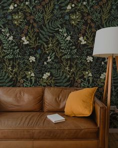 a brown leather couch sitting in front of a wallpapered with flowers and leaves