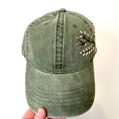 Hand embroidered green hat with floral design spread across side of hat. Adjustable strap to fit all sizes with ponytail opening in back. 6in. hat depth Hand wash to preserve quality. Adjustable Green Dad Hat With Curved Brim, Khaki Visor Hat For Spring, Green Adjustable Dad Hat With Curved Brim, Green Curved Bill Hat For Spring, Green Visor Hats For Spring, Green Adjustable Curved Bill Hat, Adjustable Hats With Floral Embroidery And Curved Bill, Green Adjustable Trucker Hat For Spring, Green Fitted Cap One Size Fits Most