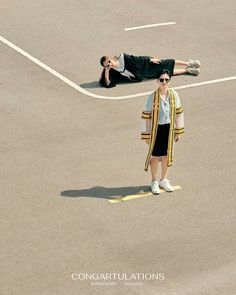 a person laying on the ground in an empty parking lot next to another person wearing sunglasses