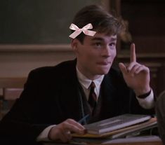 a young man sitting at a table in front of a book and pointing to the side