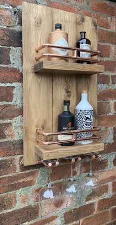 two wooden shelves with wine glasses and bottles on them next to a brick wall,