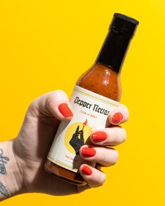 a woman holding a bottle of hot sauce in her hand on a yellow and orange background