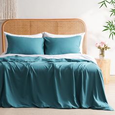 a bed with blue sheets and pillows in a room next to a potted plant