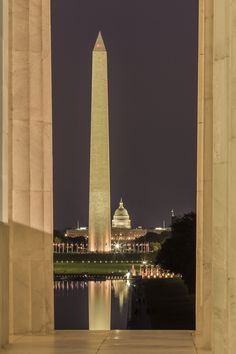 the washington monument is lit up at night with its reflection in the water behind it