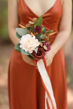 a woman in an orange dress holding a bridal bouquet with red and white flowers