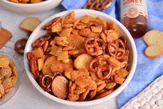 two bowls filled with cheetos and pretzels next to a bottle of honey