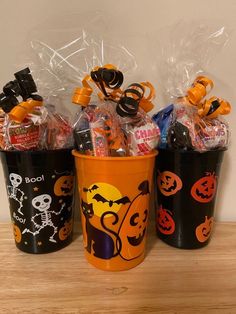 three halloween buckets with candy and candies in them on top of a wooden table