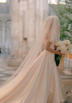 the bride is walking down the aisle with her veil blowing in the wind as she looks back