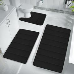 two black bath mats sitting on top of a bathroom floor next to a white toilet