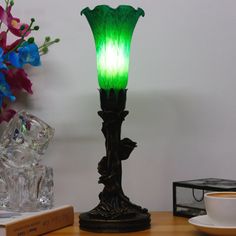 a green lamp sitting on top of a table next to a cup and saucer