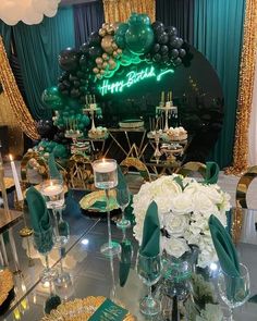 a table set up for a party with green and gold decorations, balloons and candles