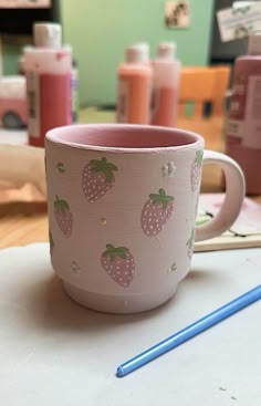 a pink cup with strawberries on it sitting on a table next to a blue pencil