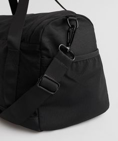 a black duffel bag on a white surface with the strap hanging down to it's side